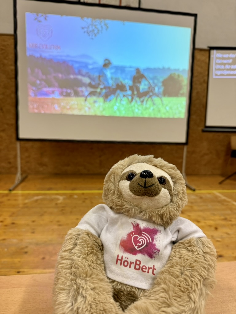 HörBert-Maskottchen vor einer Präsentation von Kids Evolution
